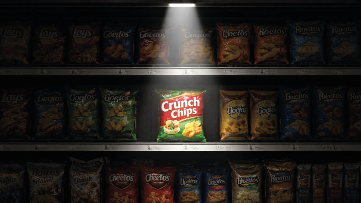 Una ripresa cinematografica di uno scaffale di snack in un supermercato scarsamente illuminato. Un unico pacchetto di "Crunch Chips" al centro è investito da un fascio di luce zenitale (spotlight) che lo isola completamente dagli altri prodotti sfuocati e in ombra. L'immagine rappresenta visivamente il concetto di Visual Salience (Gerarchia dell'Attenzione).